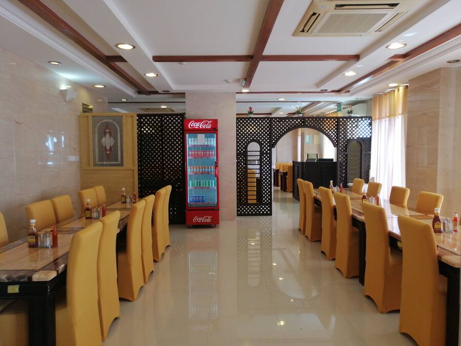 A restaurant with multiple dining tables and chairs, a Coca-Cola refrigerator, and a decorative wall with an archway.