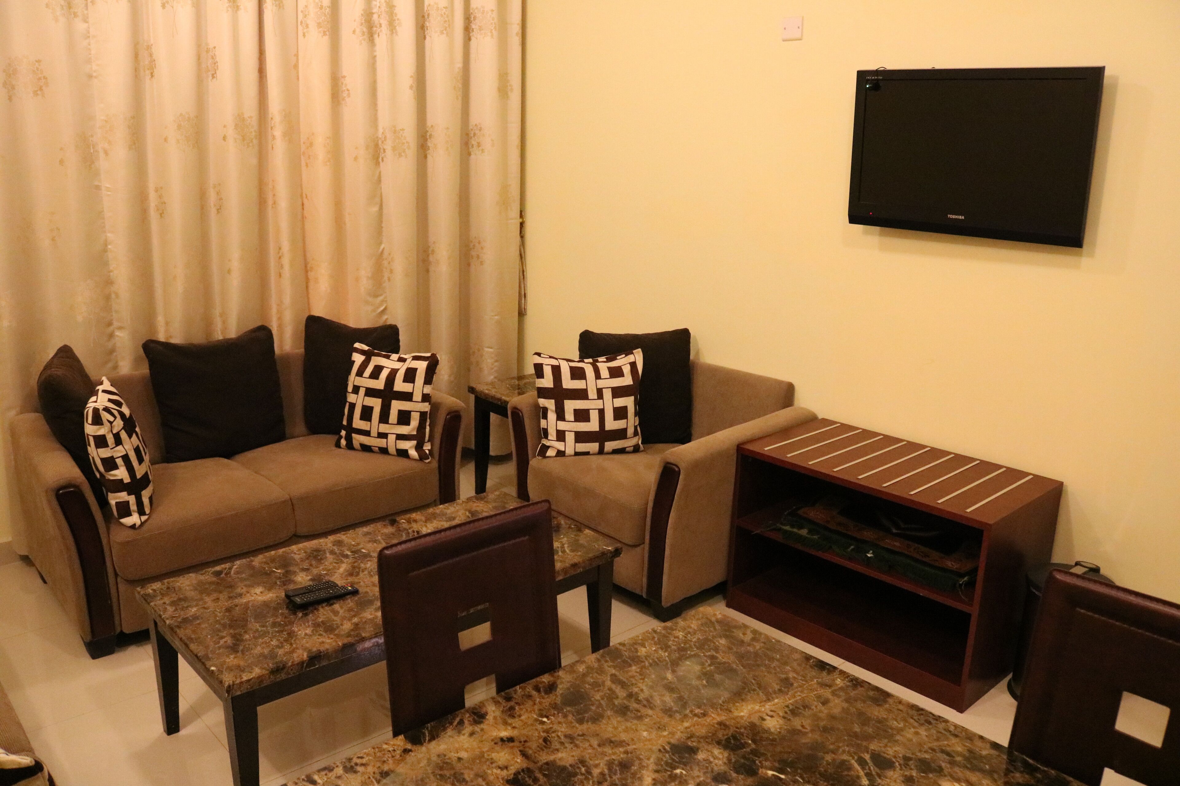 A living room with a sofa, two armchairs, a coffee table, and a flat-screen TV mounted on the wall.