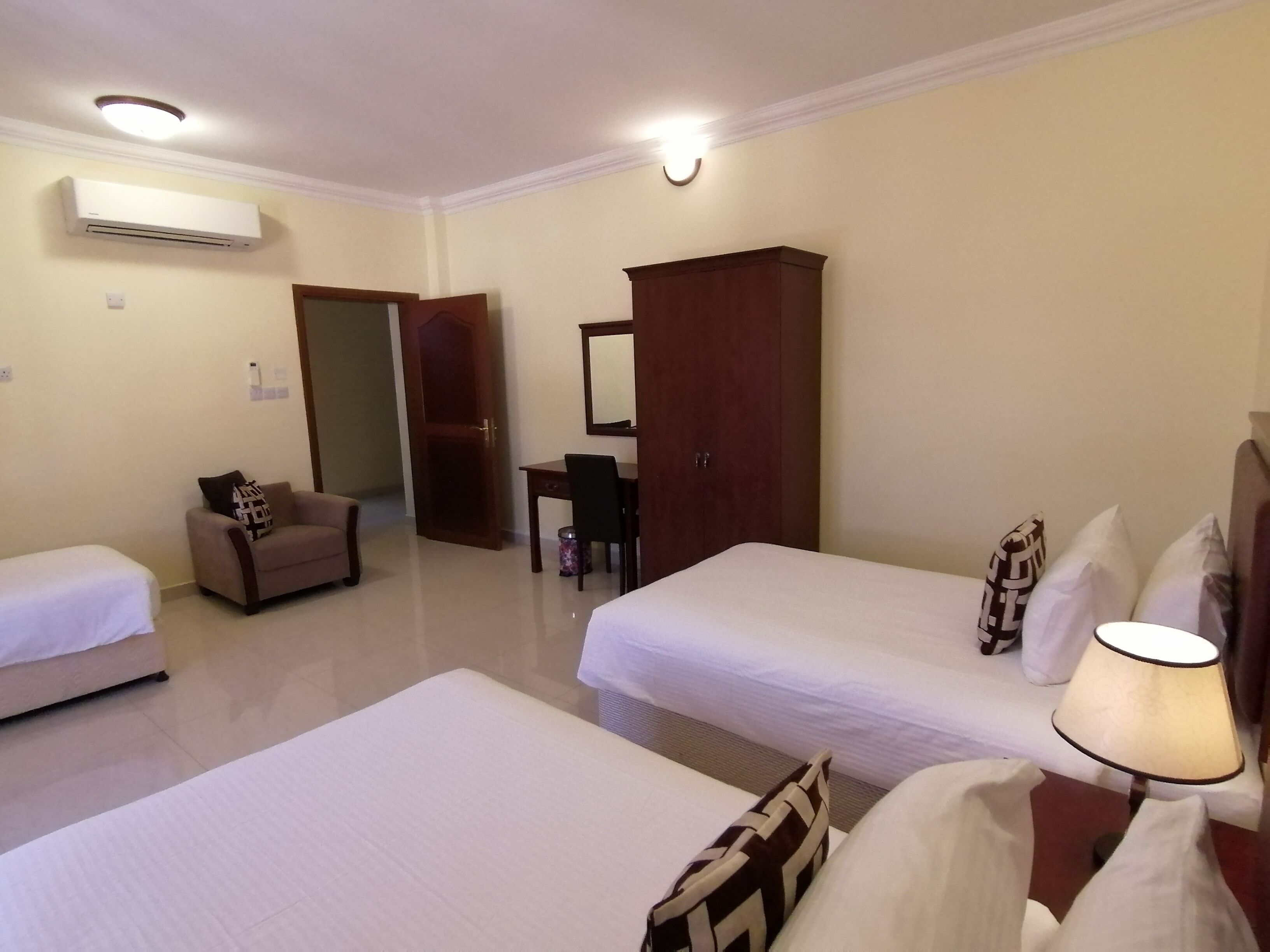 A hotel room with two single beds, a desk, a chair, a wardrobe, and an air conditioning unit.