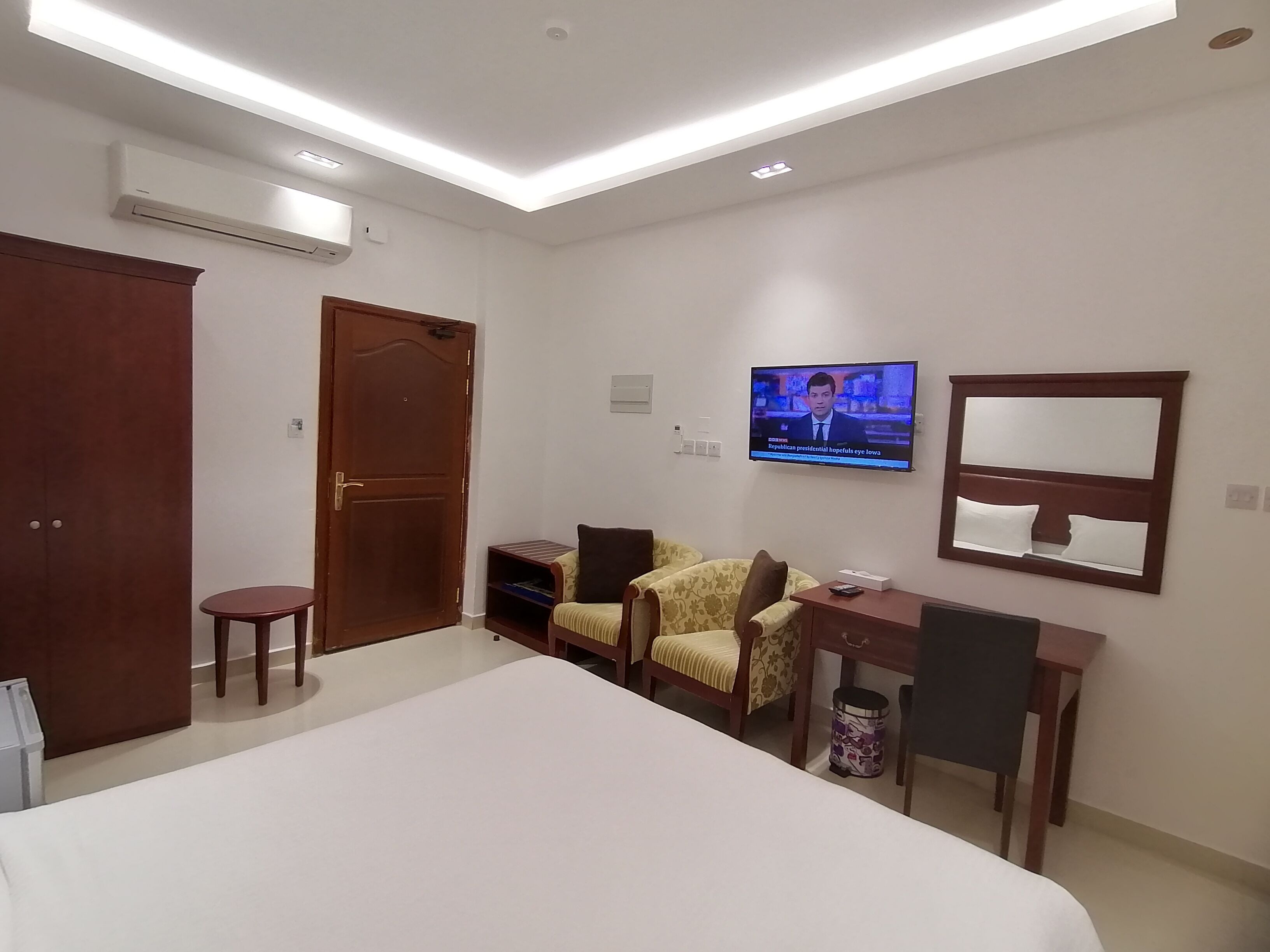 Una habitación de hotel con cama, escritorio, silla, televisor y armario.