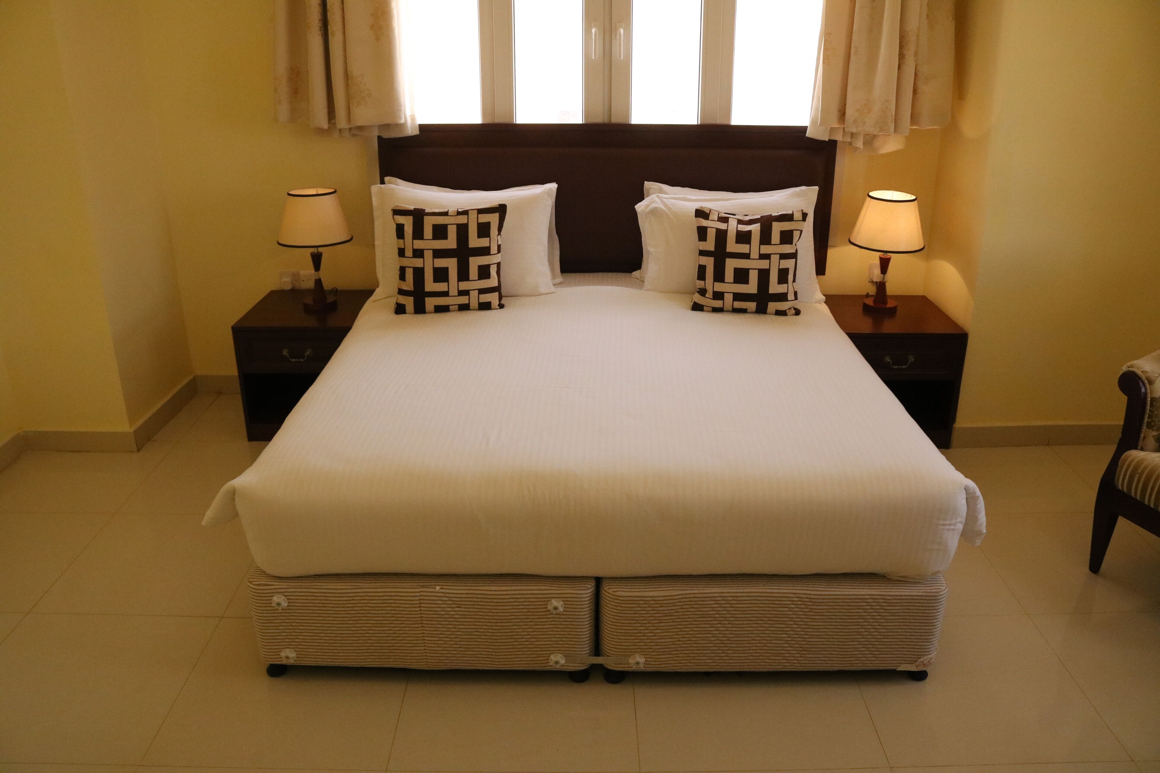 A large bed with a headboard, two bedside tables with lamps, and a chair.