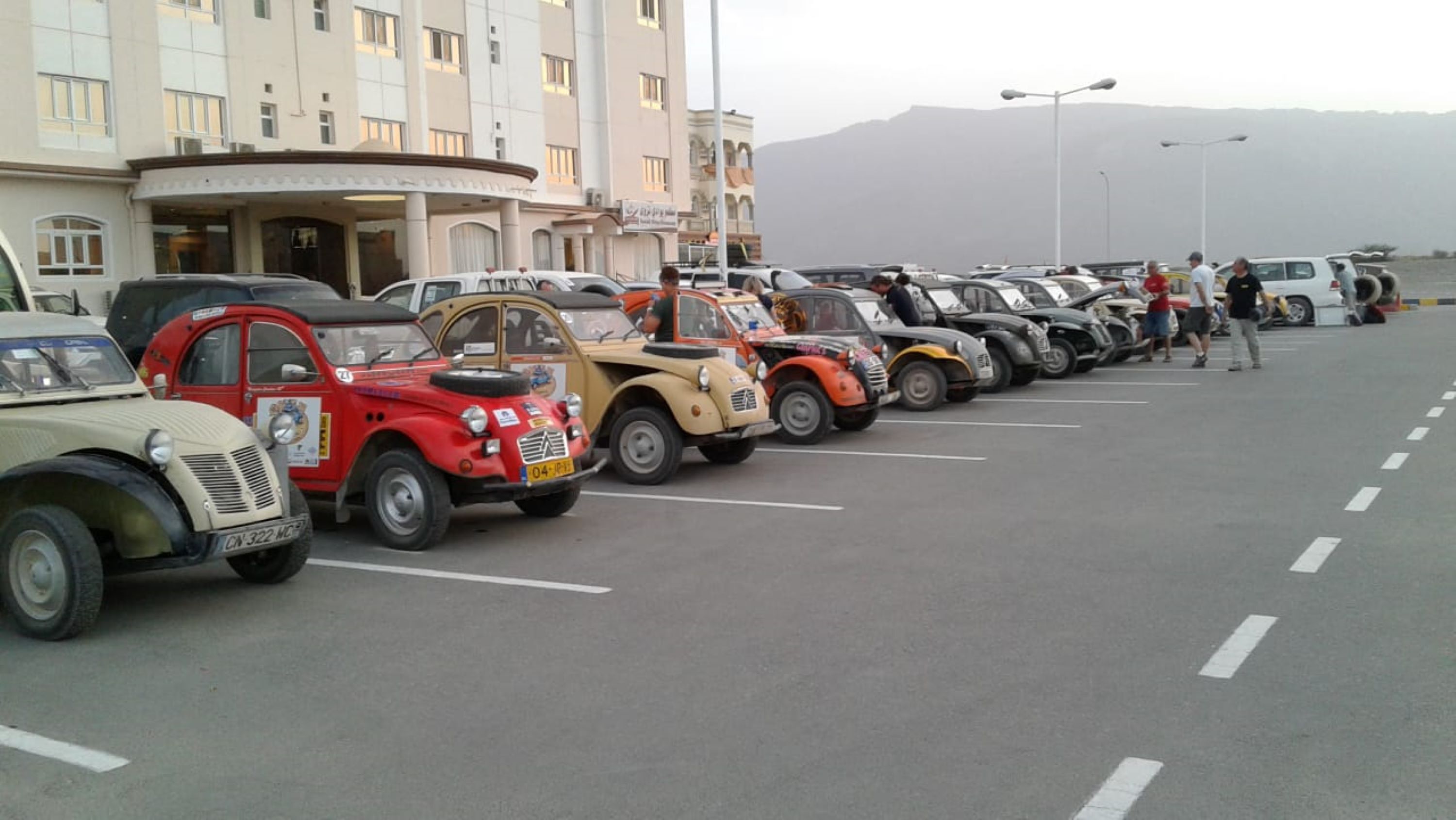 A row of vintage cars parked in a lot with a building in the background.