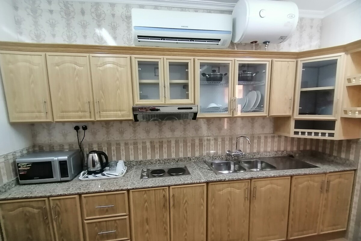 Een keuken met houten kastjes, een magnetron, een fornuis en een spoelbak.
