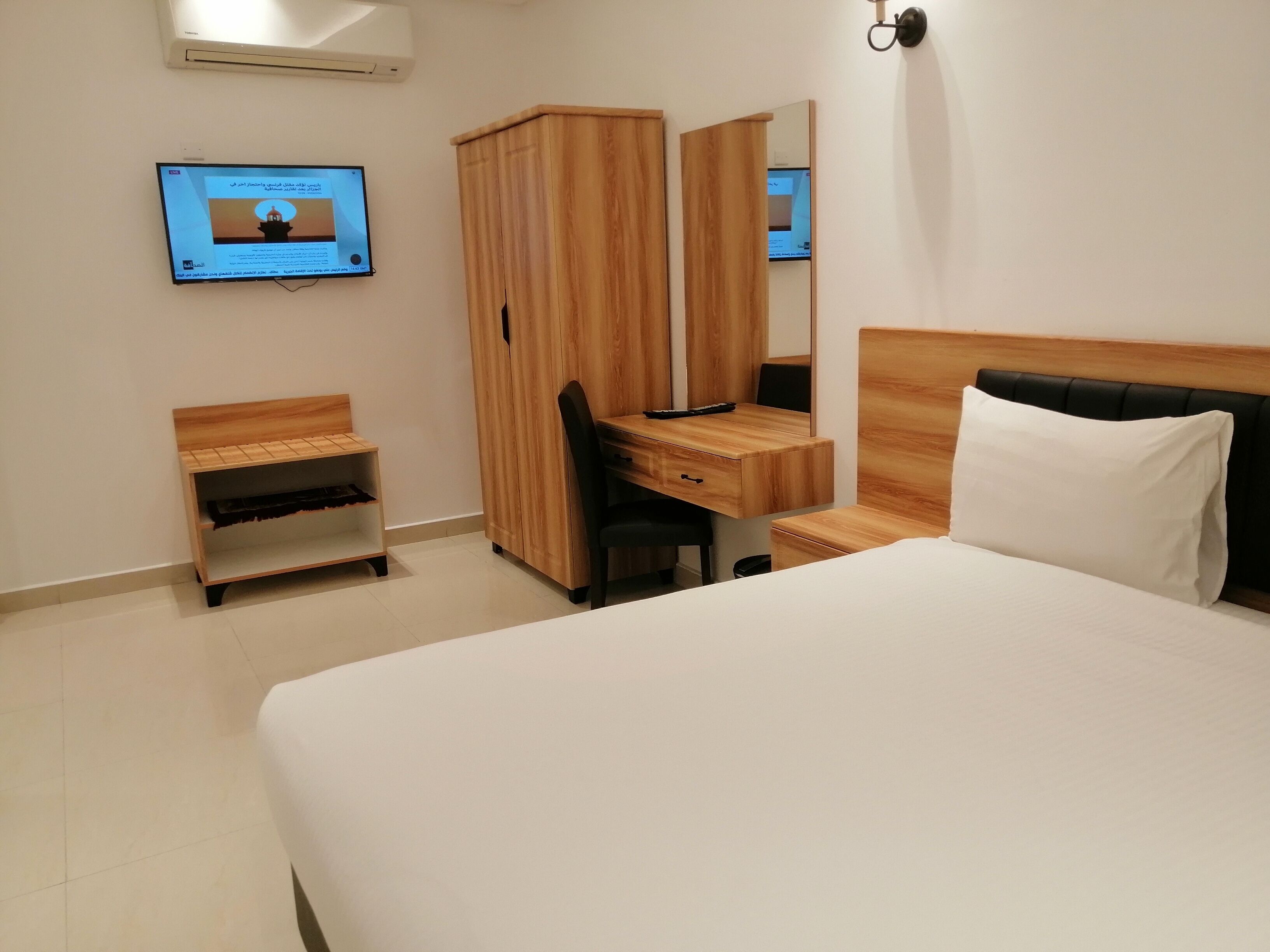 A hotel room with a bed, a wooden desk, a chair, a wardrobe, and a TV on the wall.