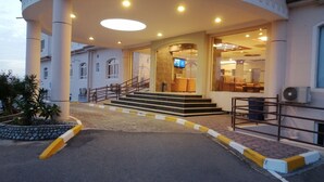 Entrada d'hotel amb una zona coberta circular, escales que condueixen a l'entrada i una porta de vidre.