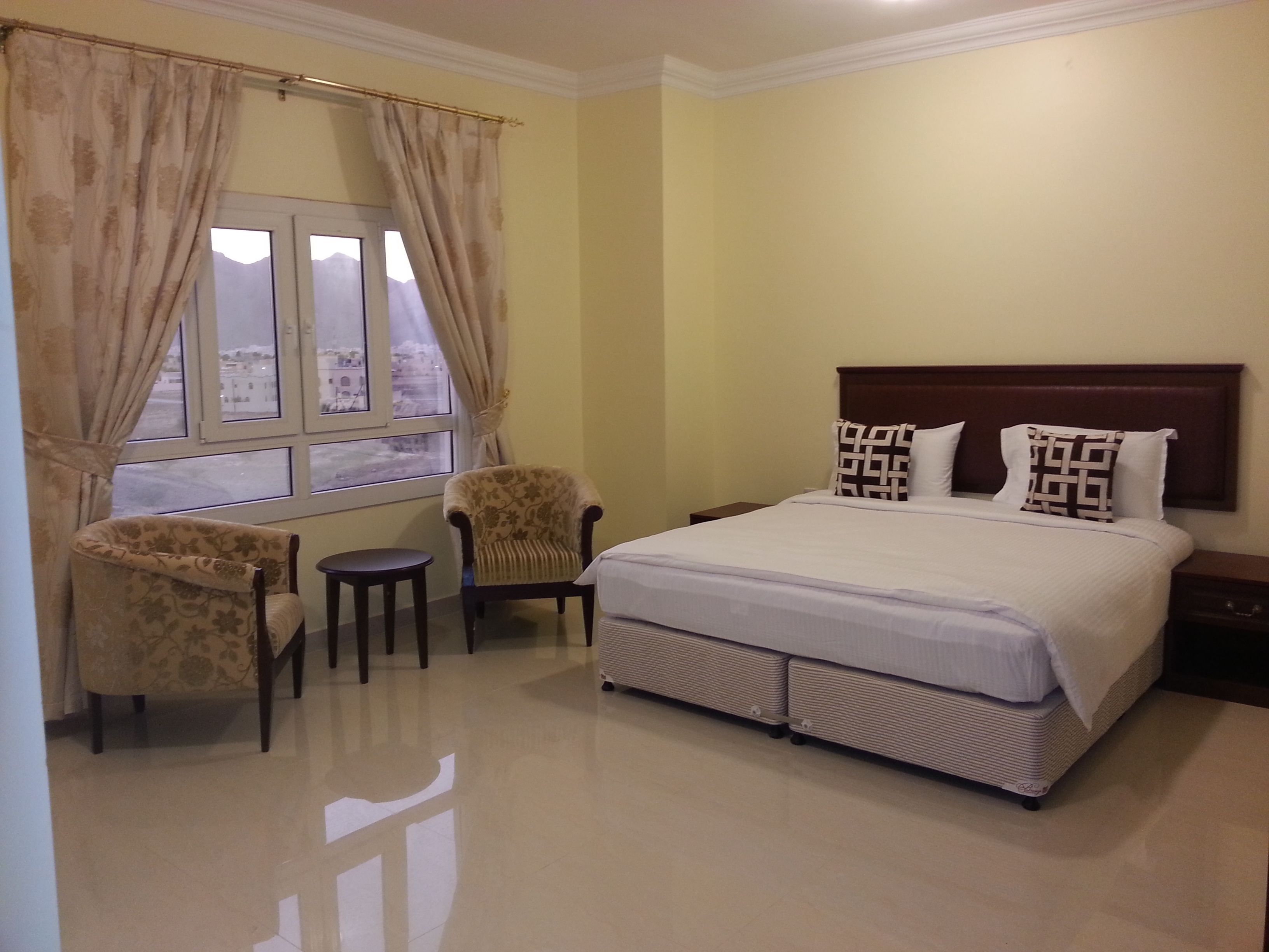 Una habitación de hotel con una cama, dos sillones, una mesita y una ventana con cortinas.