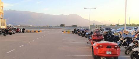 A parking lot with motorcycles and a red car, with mountains in the background.