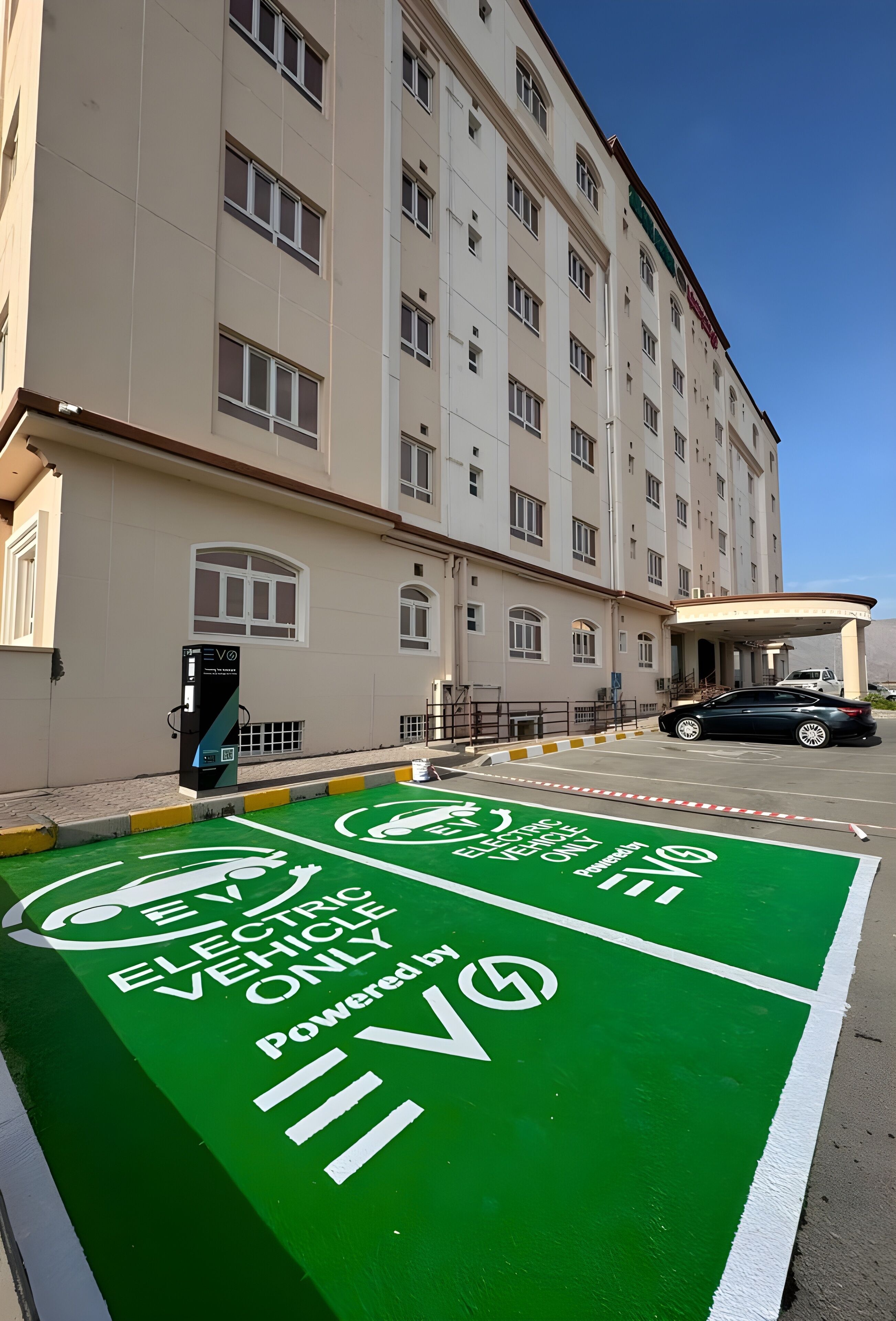 Een parkeerplaats met laadpalen voor elektrische voertuigen en een gebouw met veel ramen.
