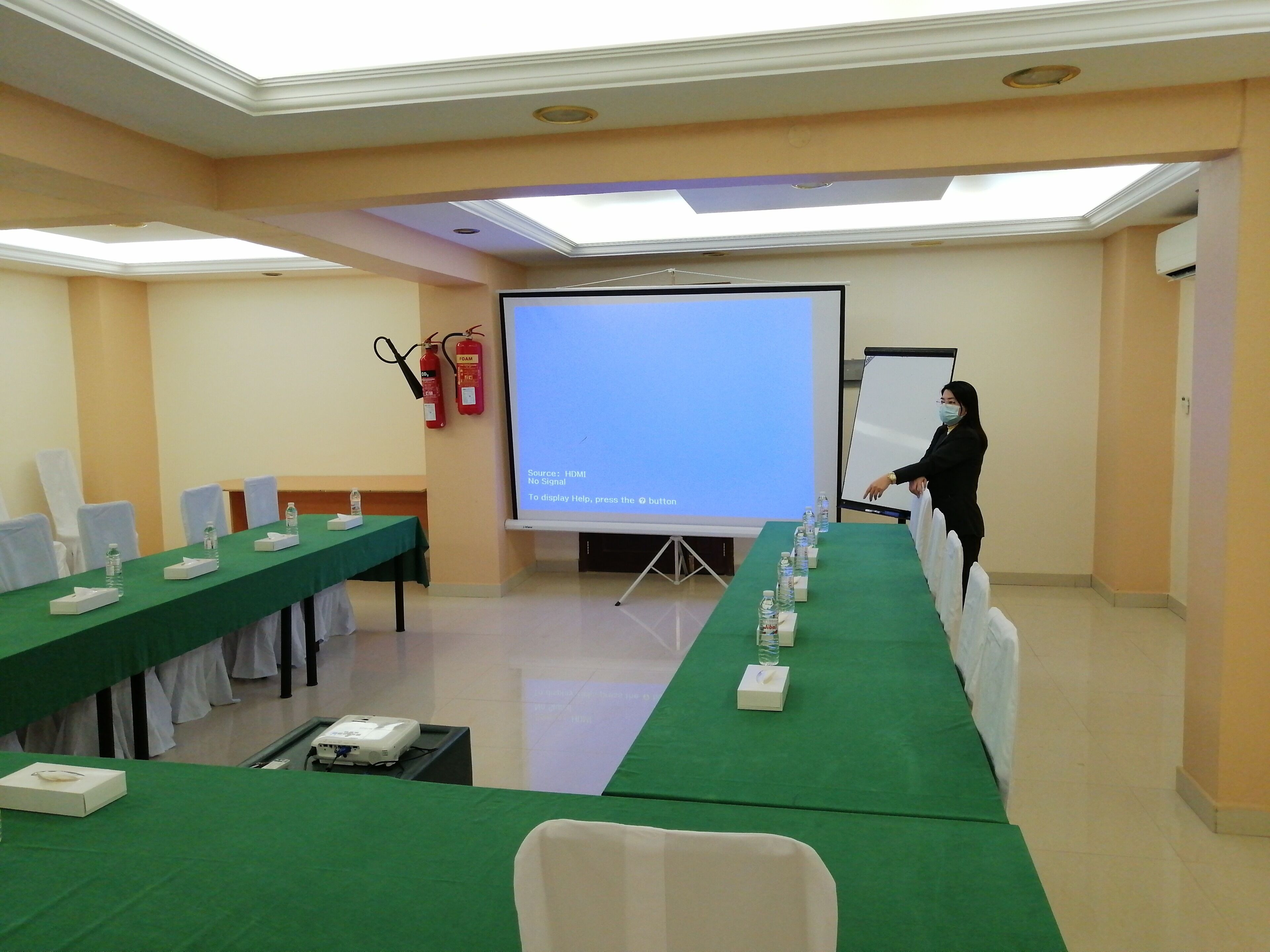 A conference room with a long table, chairs, a projector, and a screen displaying a message.