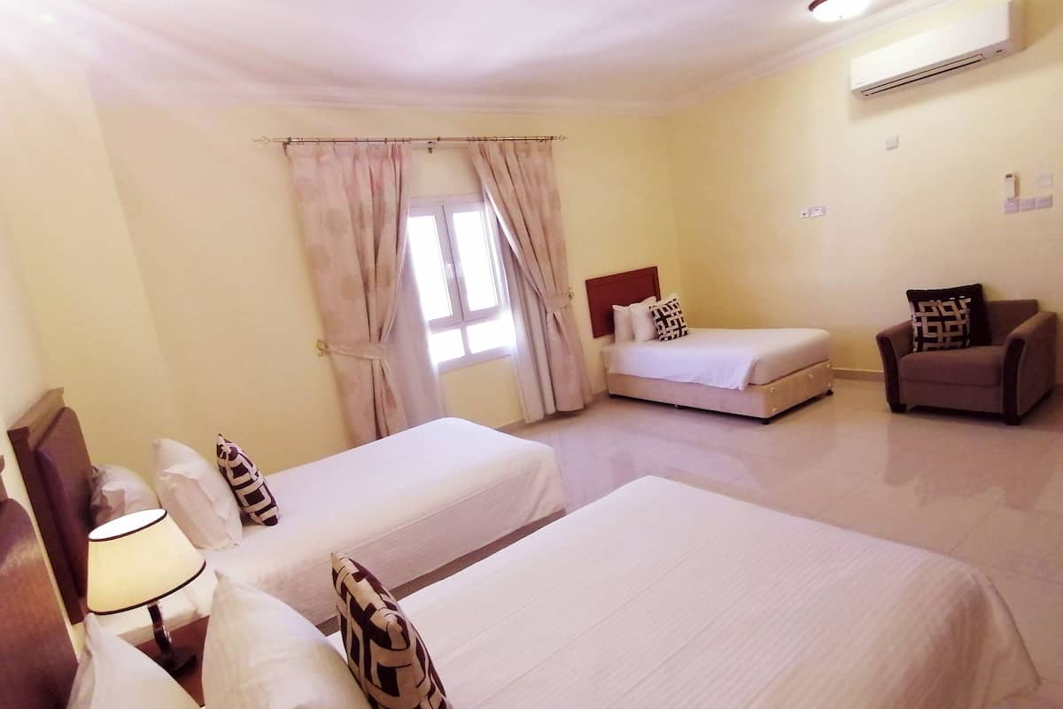 A hotel room with two beds, a chair, a lamp, and an air conditioning unit.
