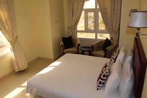 A hotel room with a large bed, a small round table, two armchairs, and a window with curtains. - Nizwa Hotel Apartments (Nizwa)