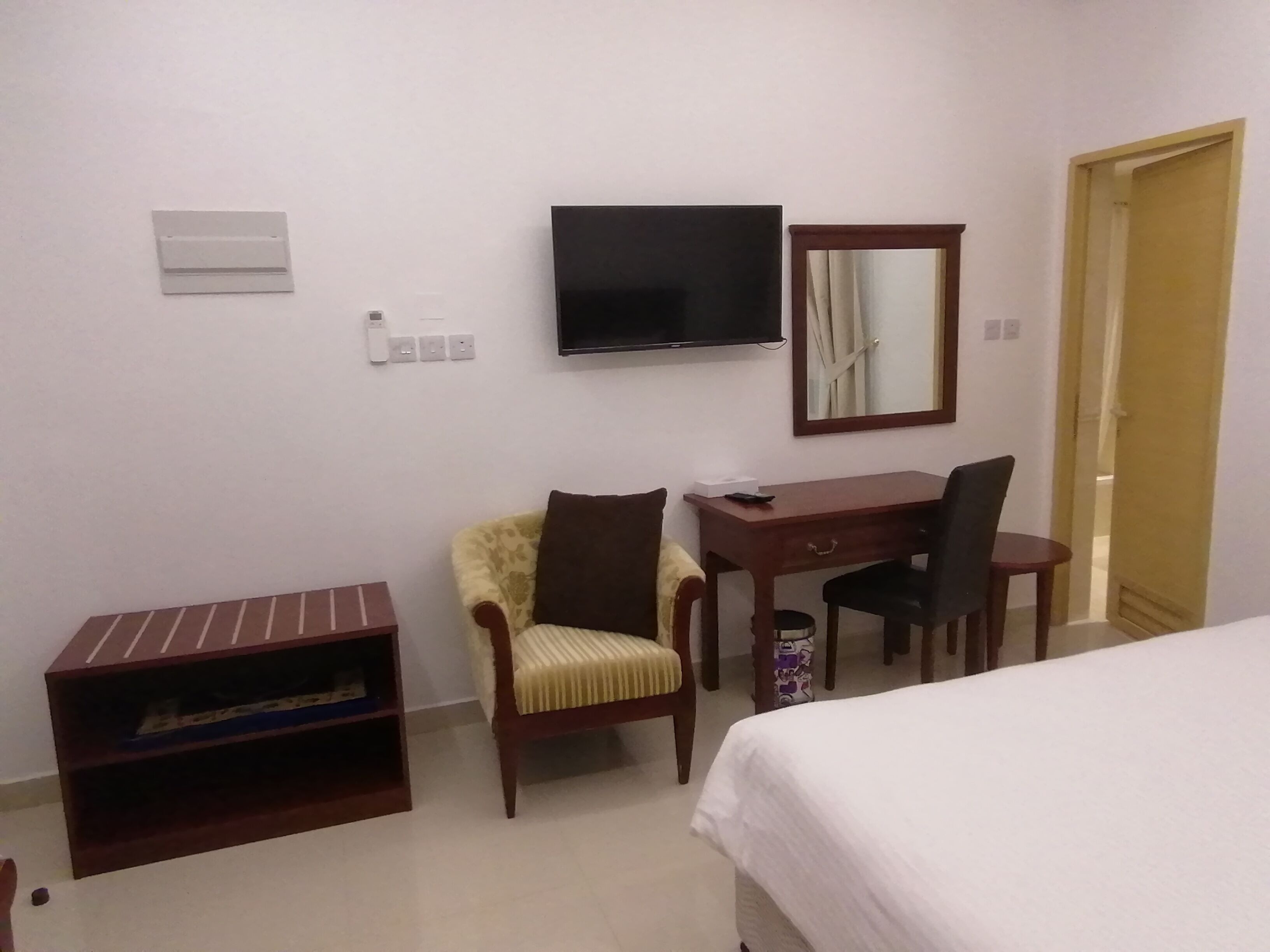 A hotel room with a bed, a desk, two chairs, a television, a mirror, and a small cabinet.