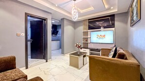 A modern living room with a sofa, coffee table, and TV. A kitchen is visible in the background. - Parkview Astoria Hotel (Lagos)