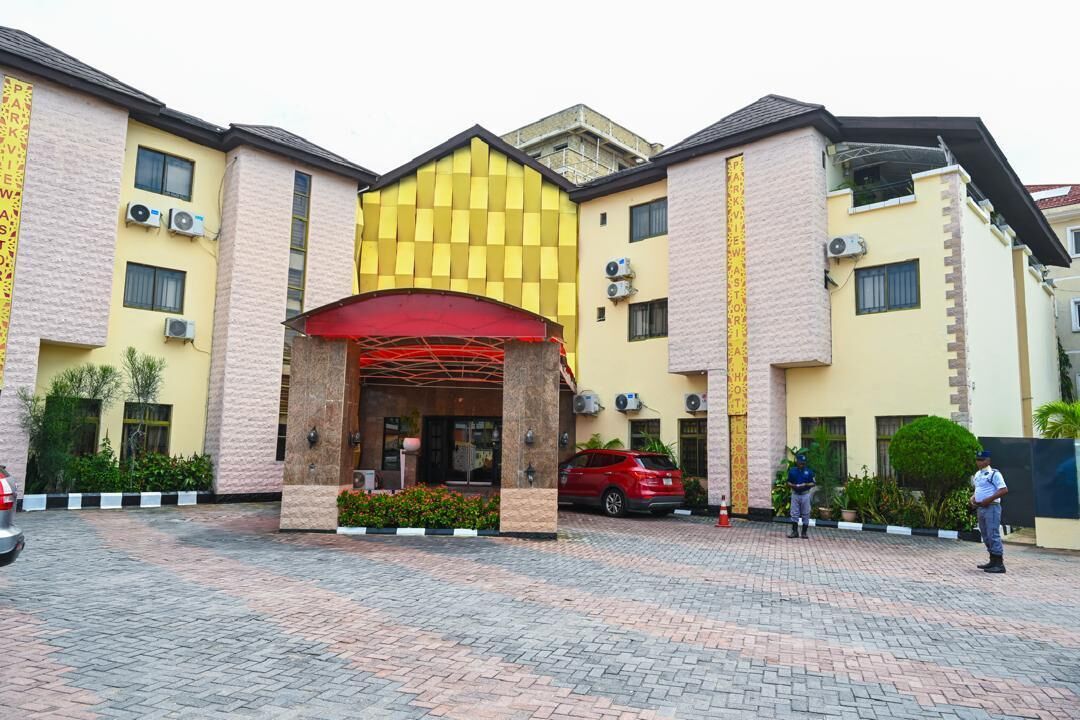 A hotel entrance with a red canopy, air conditioning units, and a paved driveway.
