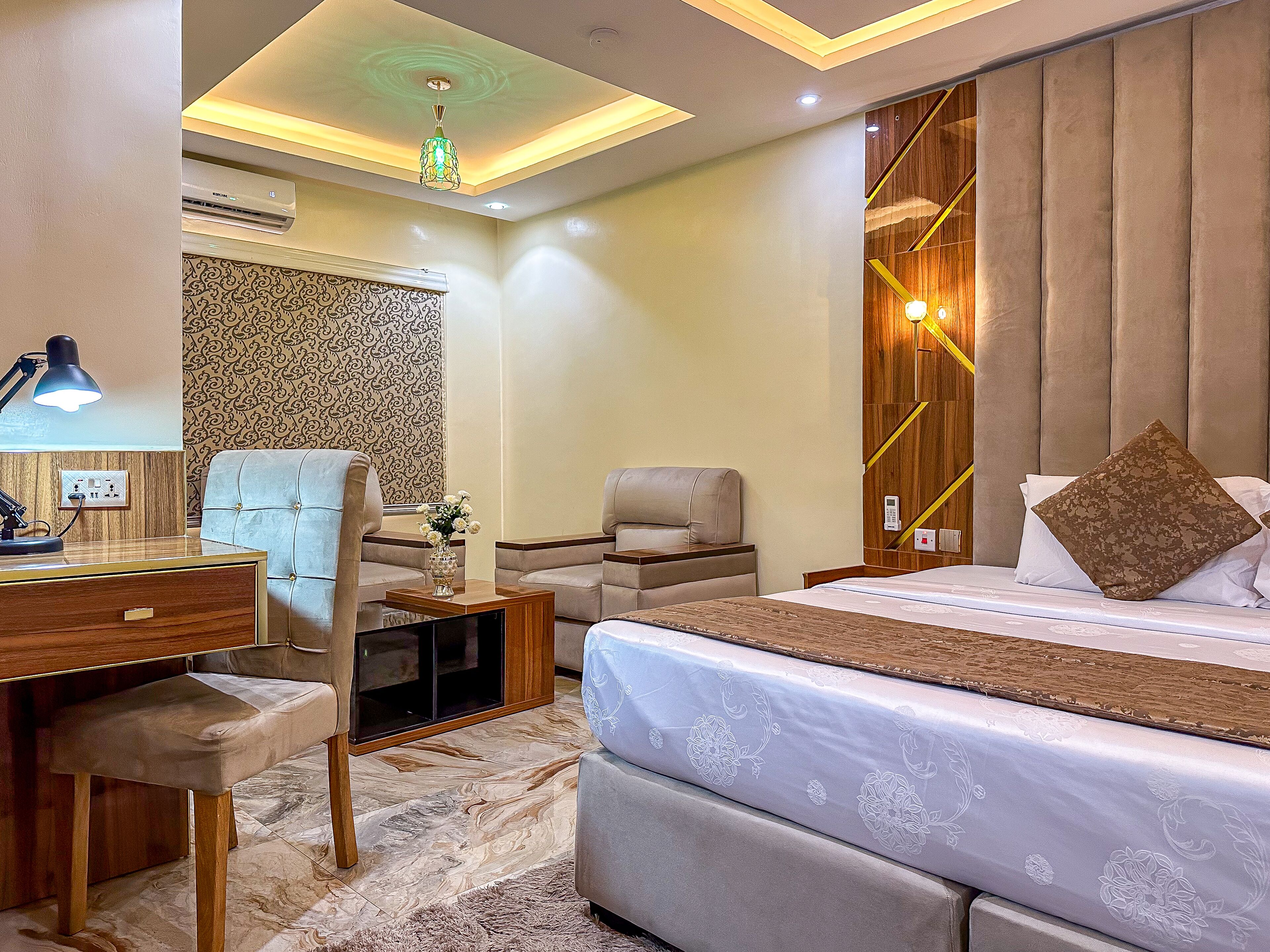 Une chambre d’hôtel moderne avec un grand lit, deux fauteuils, un bureau avec une lampe et un panneau décoratif au mur.