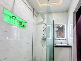 Un baño moderno con cabina de ducha de vidrio, tocador con espejo y un inodoro visible a través de un panel de vidrio.