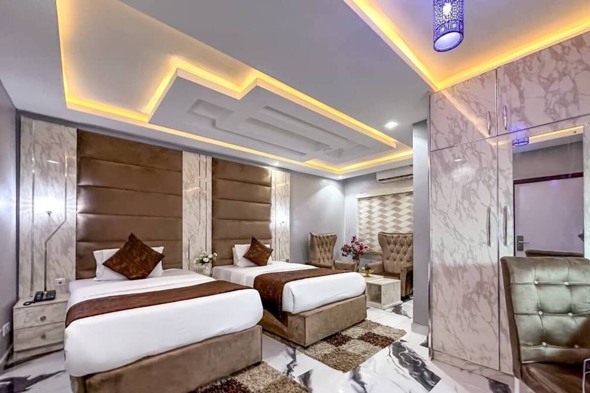 A modern hotel room with two beds, marble flooring, and a decorative ceiling light.