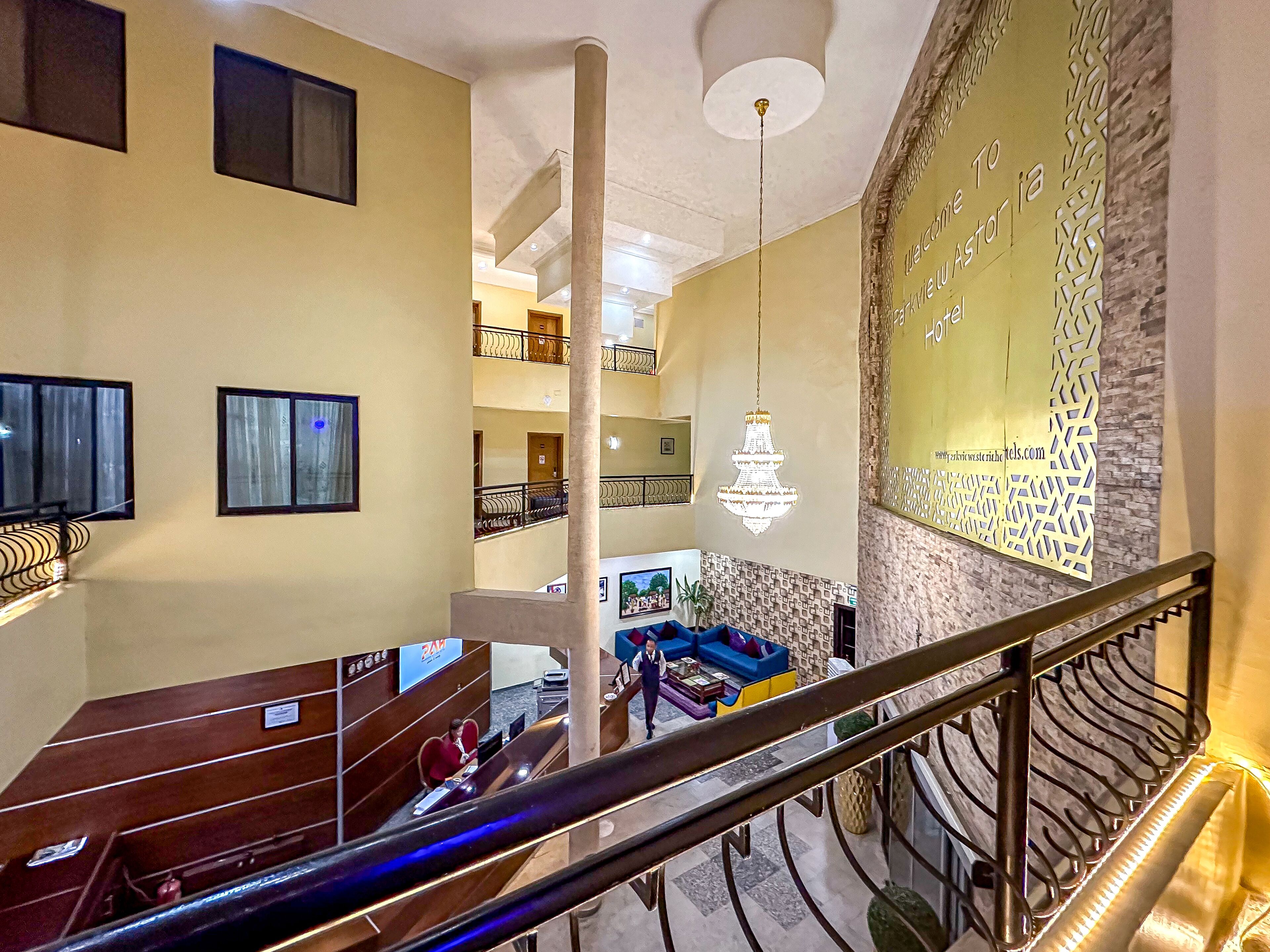 A hotel lobby with a staircase, a reception desk, a chandelier, and a decorative wall.