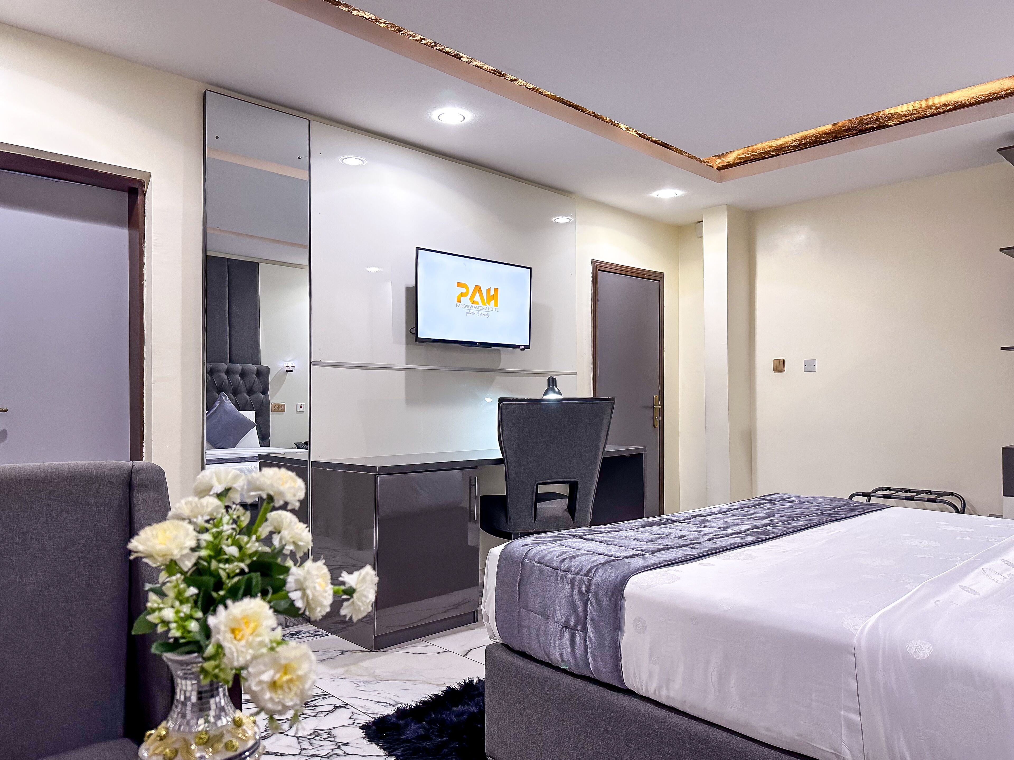 Una habitación de hotel moderna con cama, escritorio, silla y televisor en la pared.