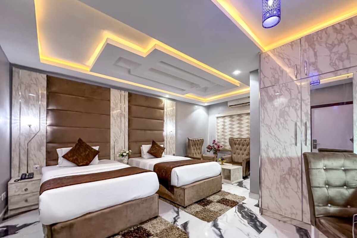 Una habitación de hotel moderna con dos camas, suelo de mármol y una lámpara decorativa en el techo.