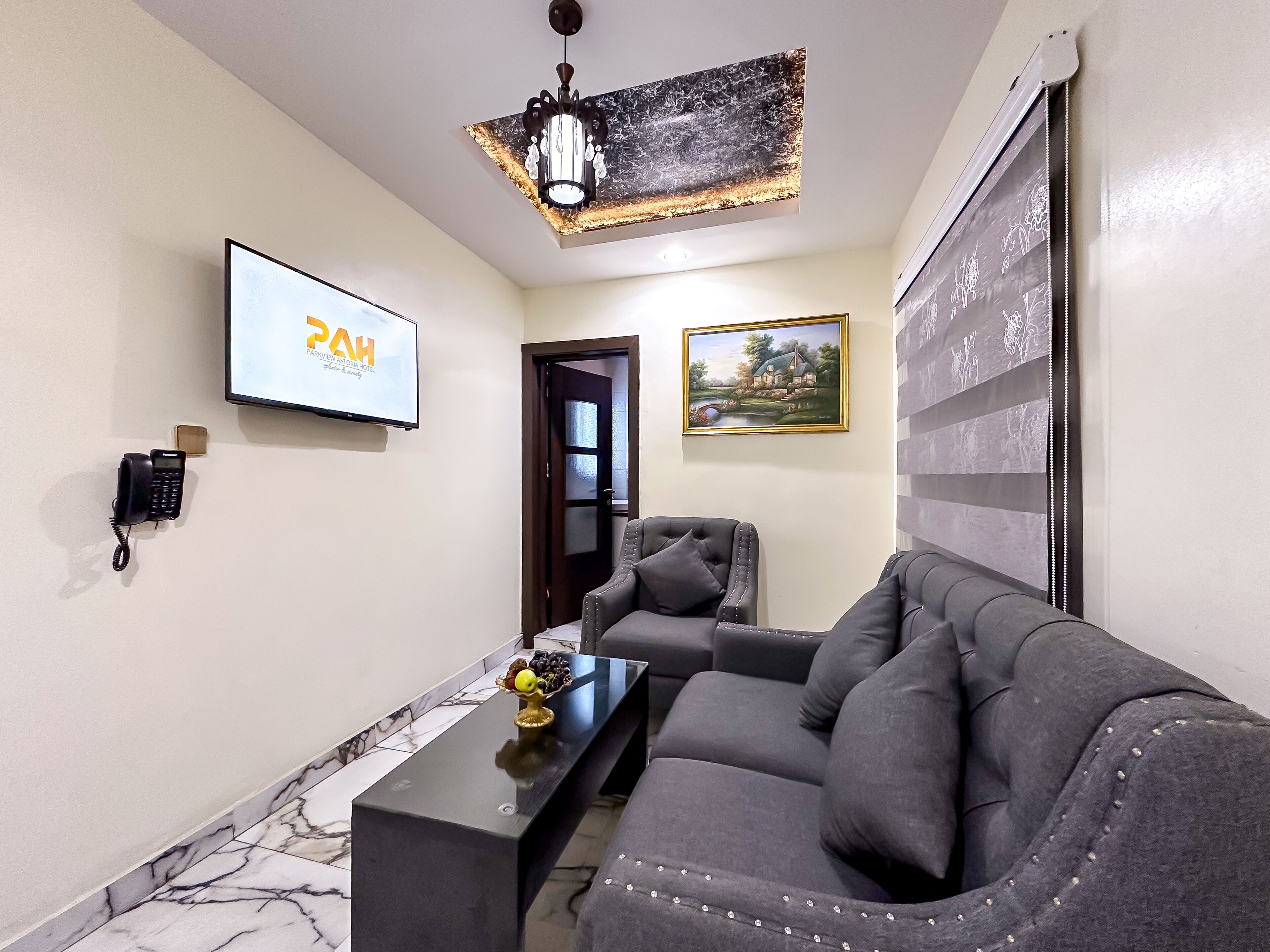 A modern living room with a grey sofa, a black coffee table, and a TV displaying a hotel name.