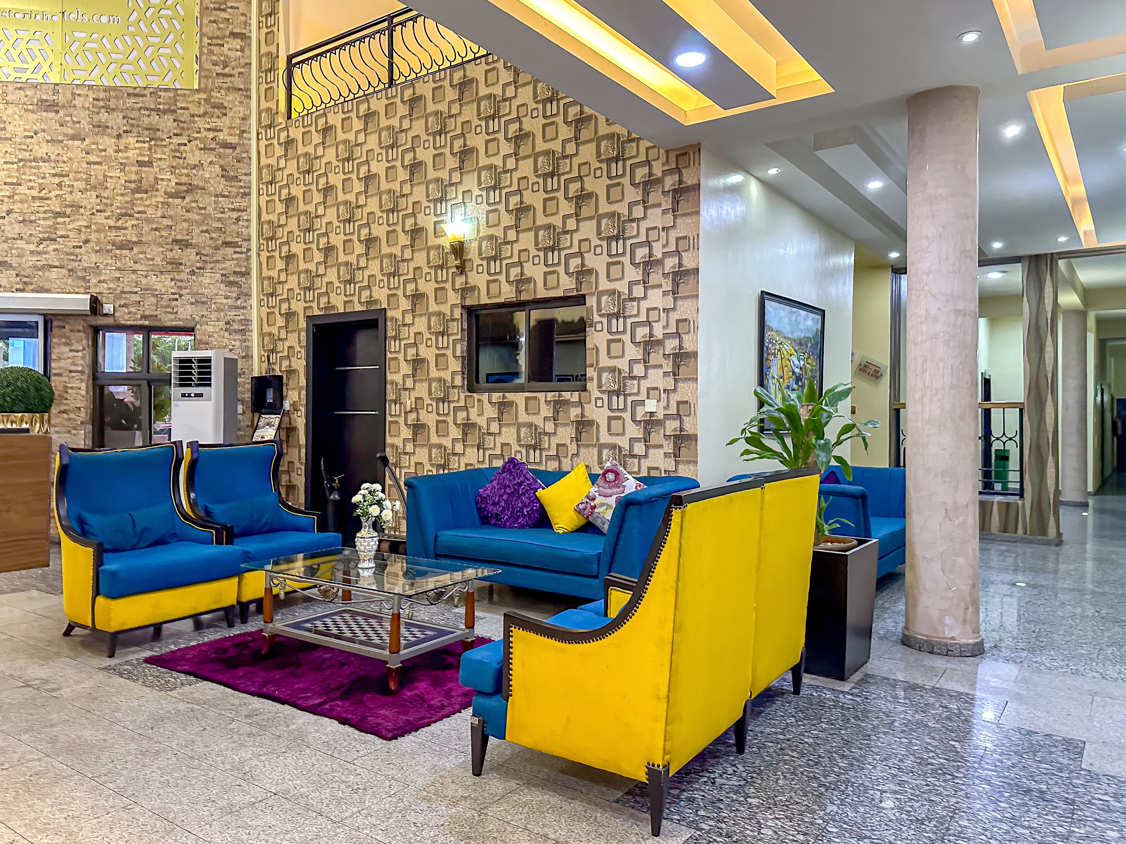 Un vestíbulo con asientos azules y amarillos, un muro con diseño y una escalera.