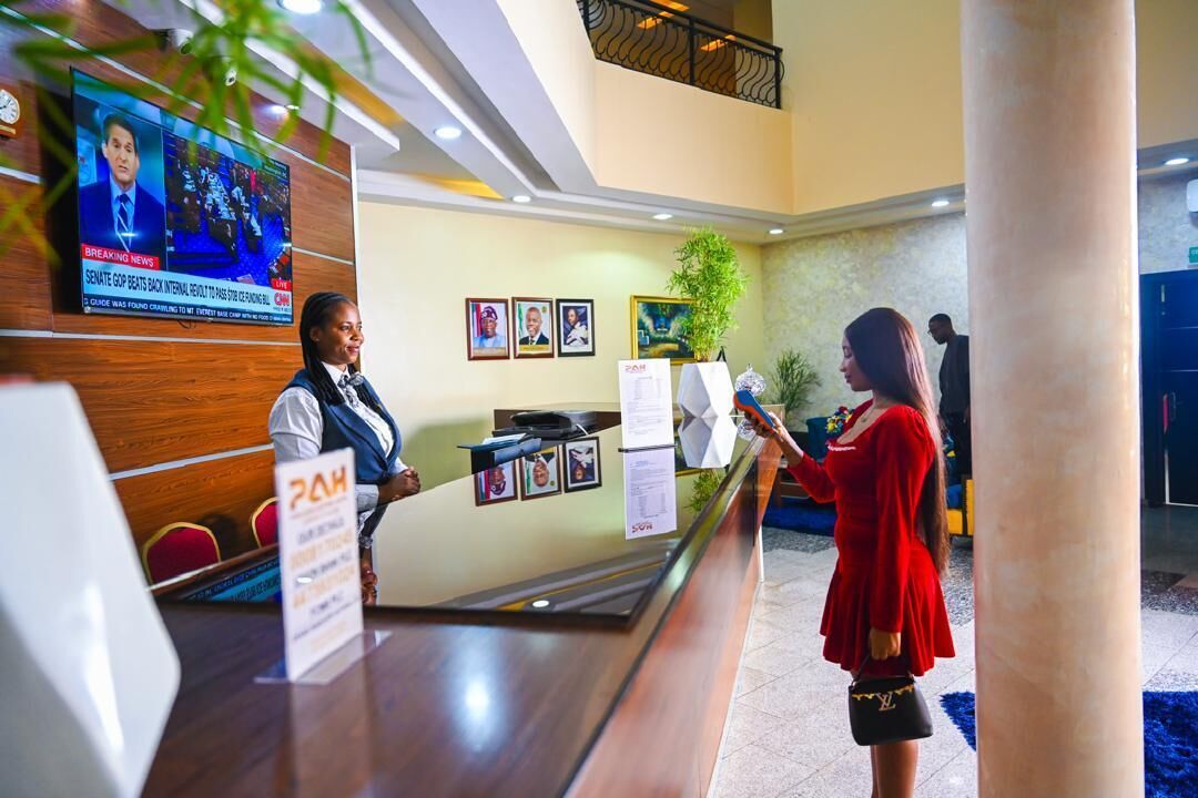 A reception desk with a television displaying news, framed photos on the wall, and a plant.