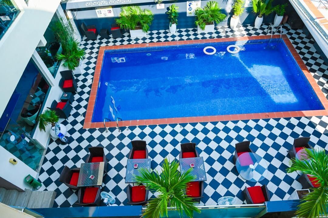 A rooftop pool with checkered flooring, lounge chairs, and potted plants.