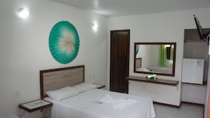 A hotel room with a bed, a nightstand, a mirror, a small table, and a refrigerator. - Pousada Camburi (Morro de Sao Paulo)