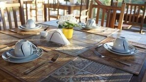 A dining table set with white plates, bowls, and cutlery, with a vase of white flowers in the center. - Pousada Camburi (Morro de Sao Paulo)