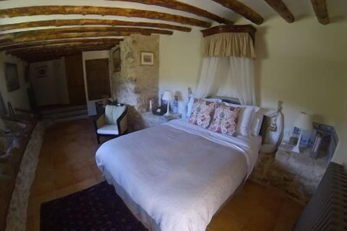 A bedroom with a large bed, a chair, a nightstand, and a stone wall.