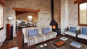Un interior rústico con pared de piedra, vigas de madera, chimenea, sofá y zona de comedor.