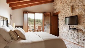 Un dormitorio con cama, televisor montado en una pared de piedra y balcón con una silla.