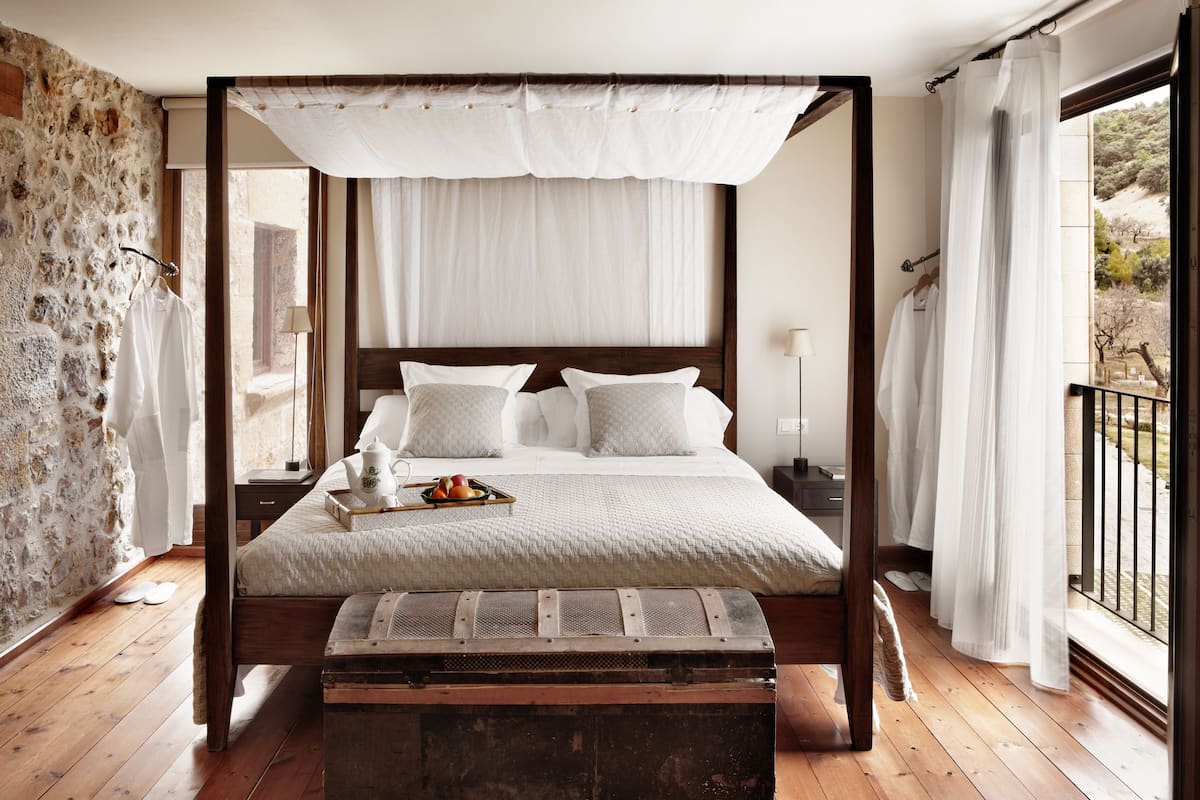 A four-poster bed with a canopy, a wooden bench, and a tray with fruit.