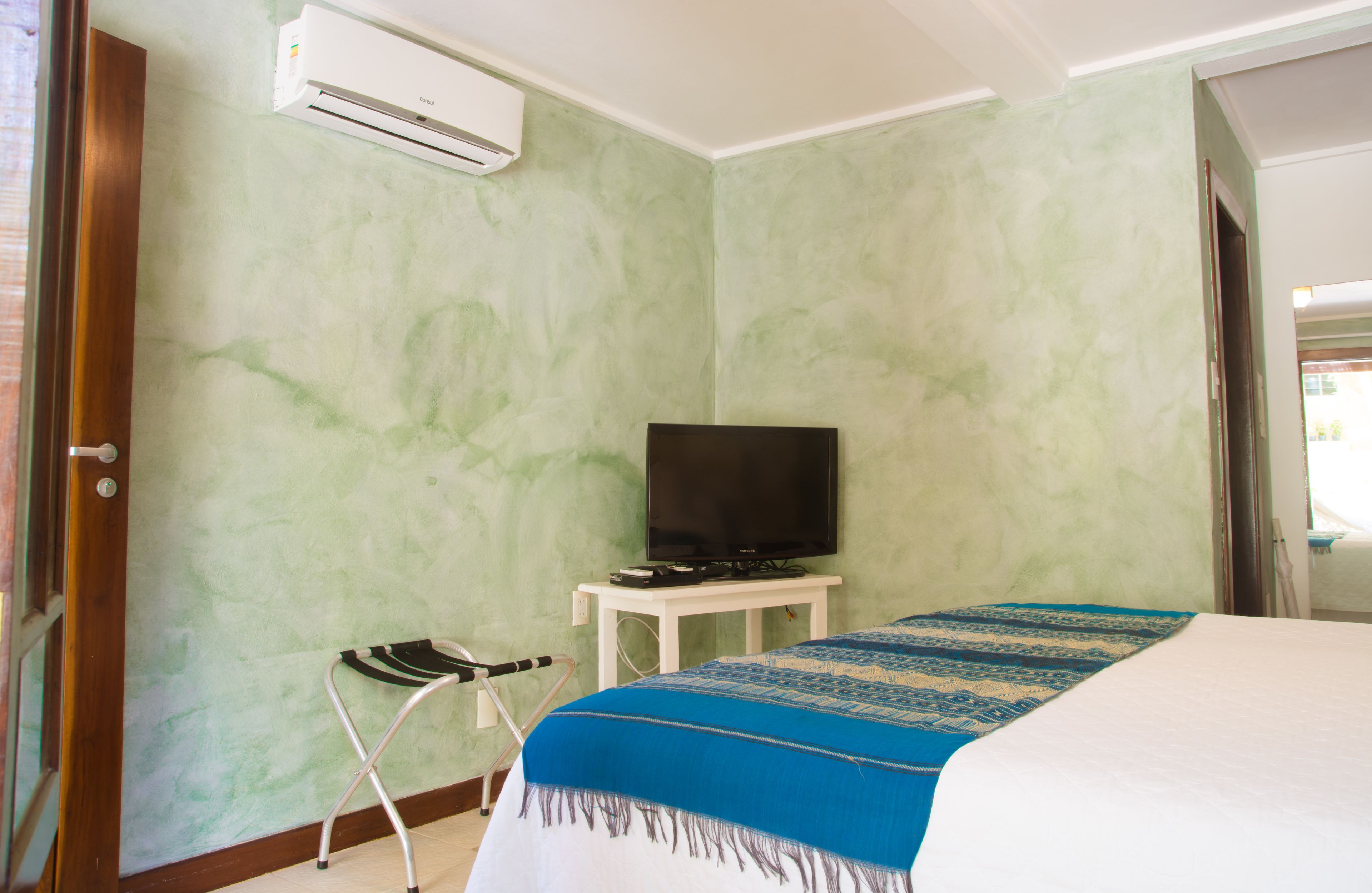 A hotel room with a bed, a television on a small table, a chair, and an air conditioning unit on the wall.