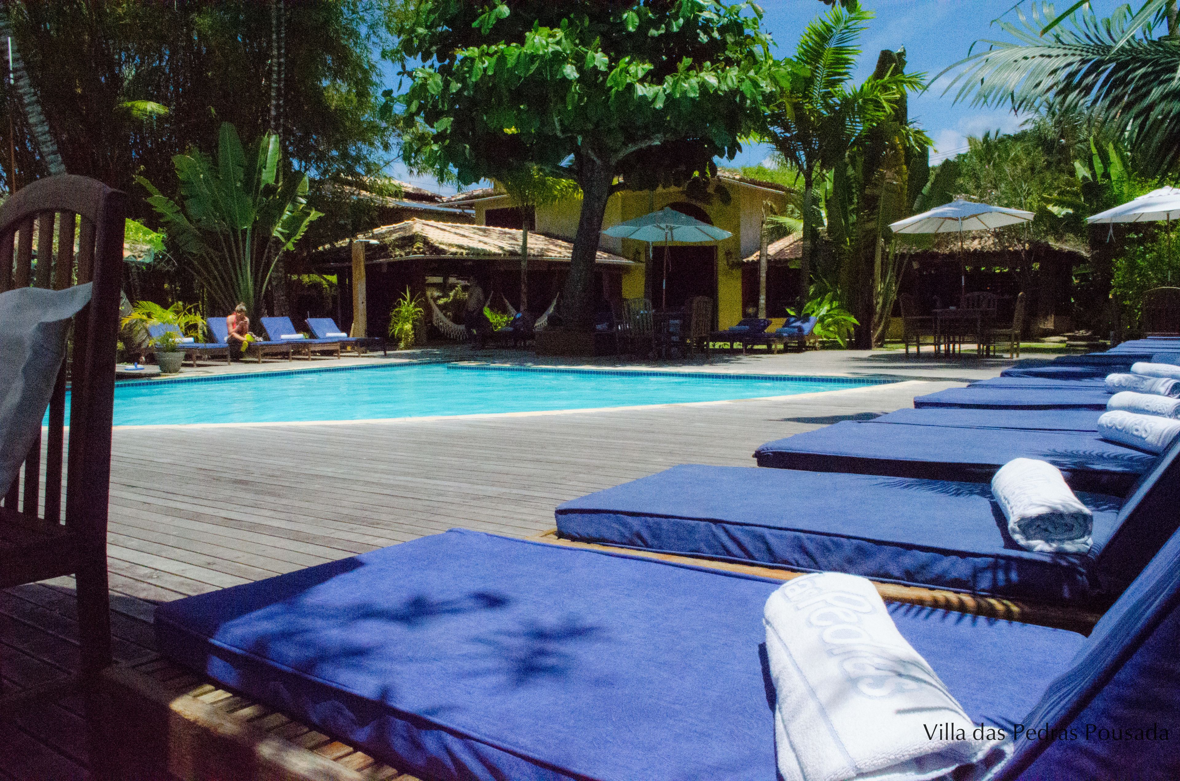 A poolside area with lounge chairs and umbrellas, surrounded by tropical plants and a wooden deck.