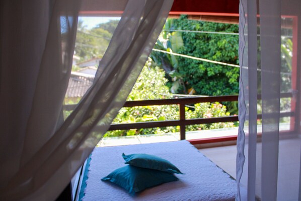 A balcony with a bed, white curtains, and a view of greenery outside. - Via das Pedras Pousada (Cairu)