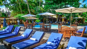 Un área junto a la piscina con sillones, sombrillas y una piscina pequeña.
