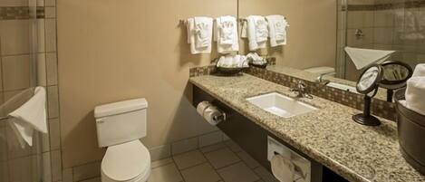 A bathroom with a toilet, two sinks, a mirror, and a shower area.