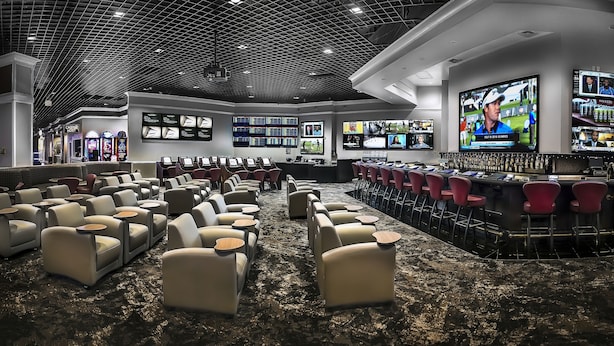 A spacious lounge area with multiple seating options, a bar with red chairs, and multiple screens displaying sports events. - Pahrump Nugget Hotel and Casino (Pahrump)