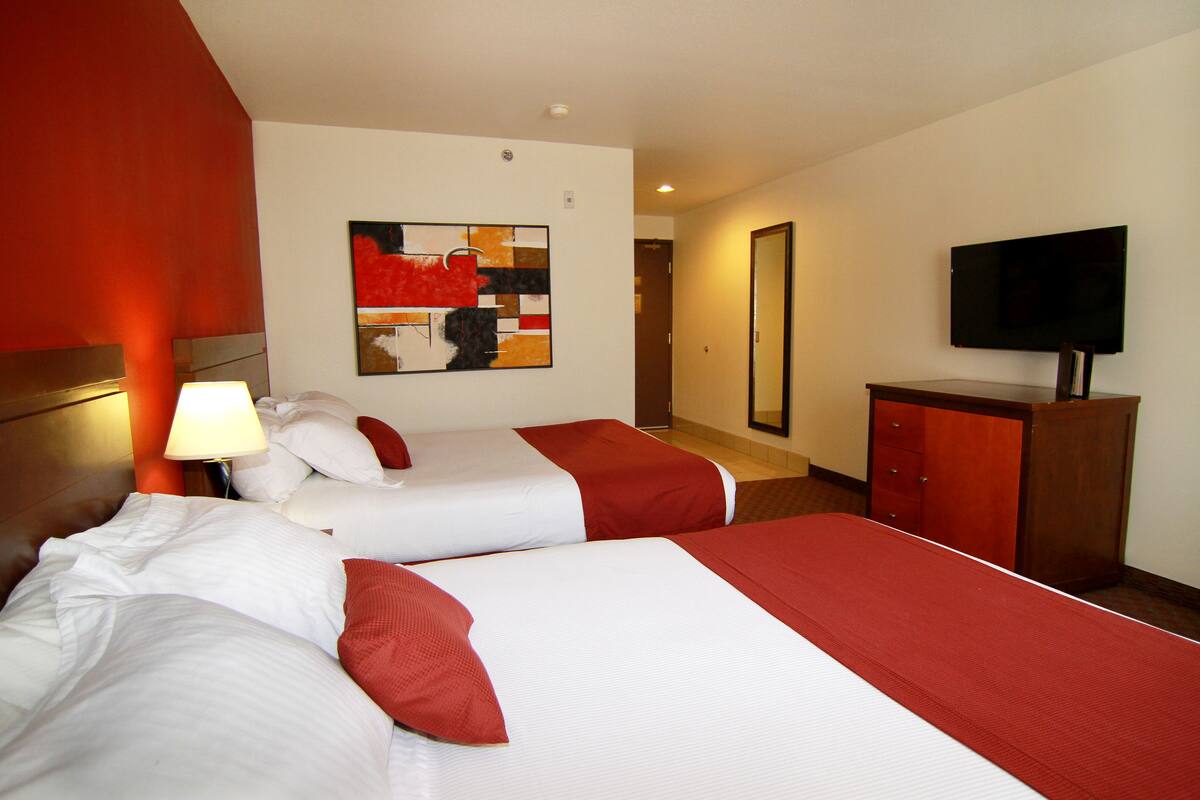 A hotel room with two beds, a TV, a painting, and a wooden cabinet.
