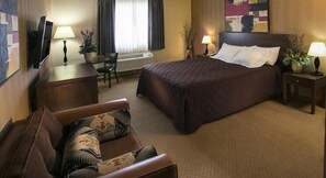 A hotel room with a bed, a sofa, a desk, a TV, and two lamps. - Pahrump Nugget Hotel and Casino (Pahrump)