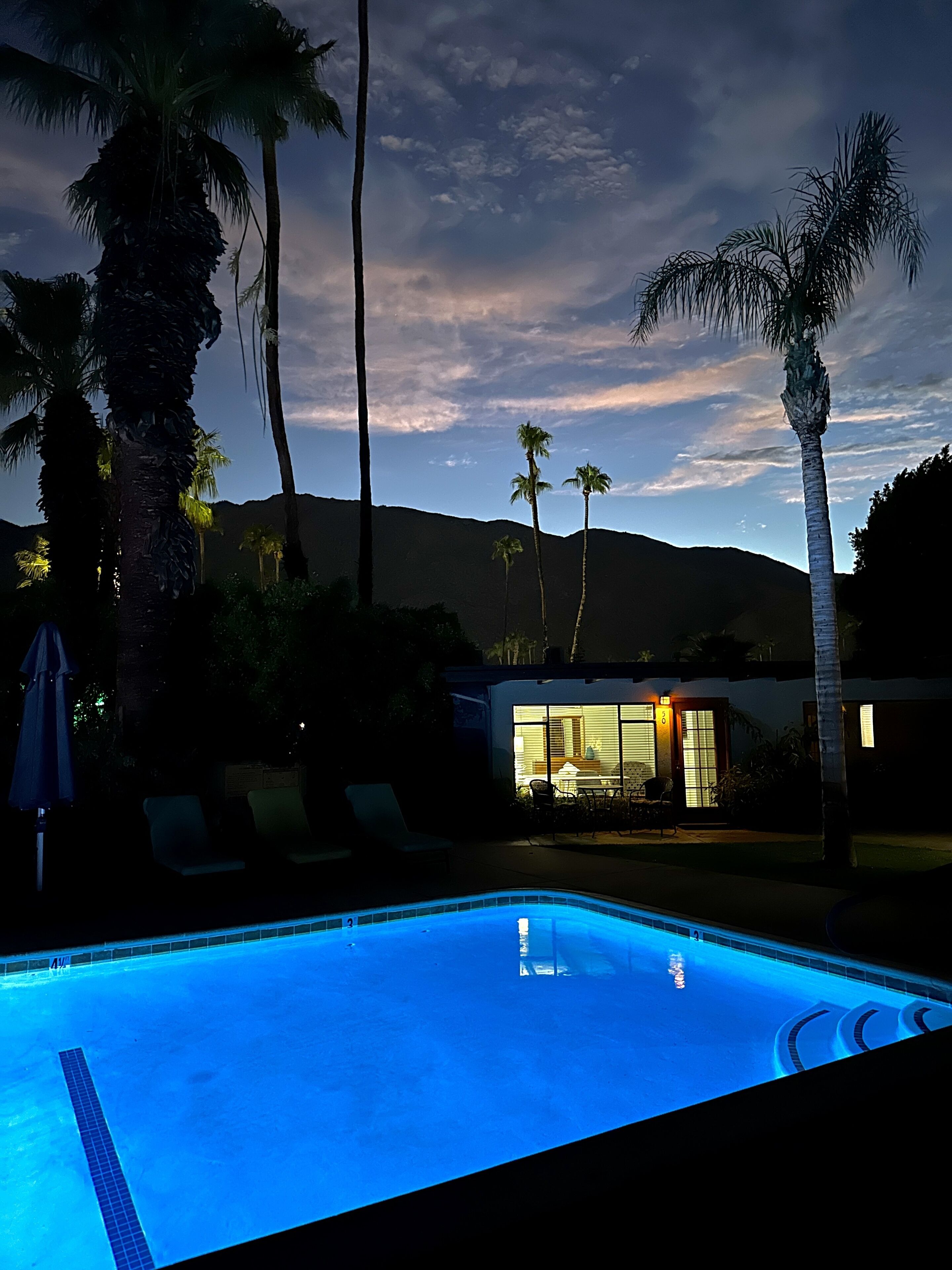 Une piscine avec des chaises longues et un bâtiment dont les fenêtres sont illuminées.