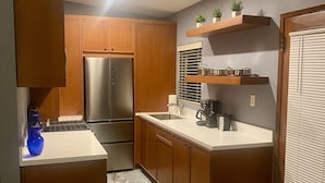 A compact kitchen with wooden cabinets, a stainless steel refrigerator, a marble countertop, and a built-in oven.