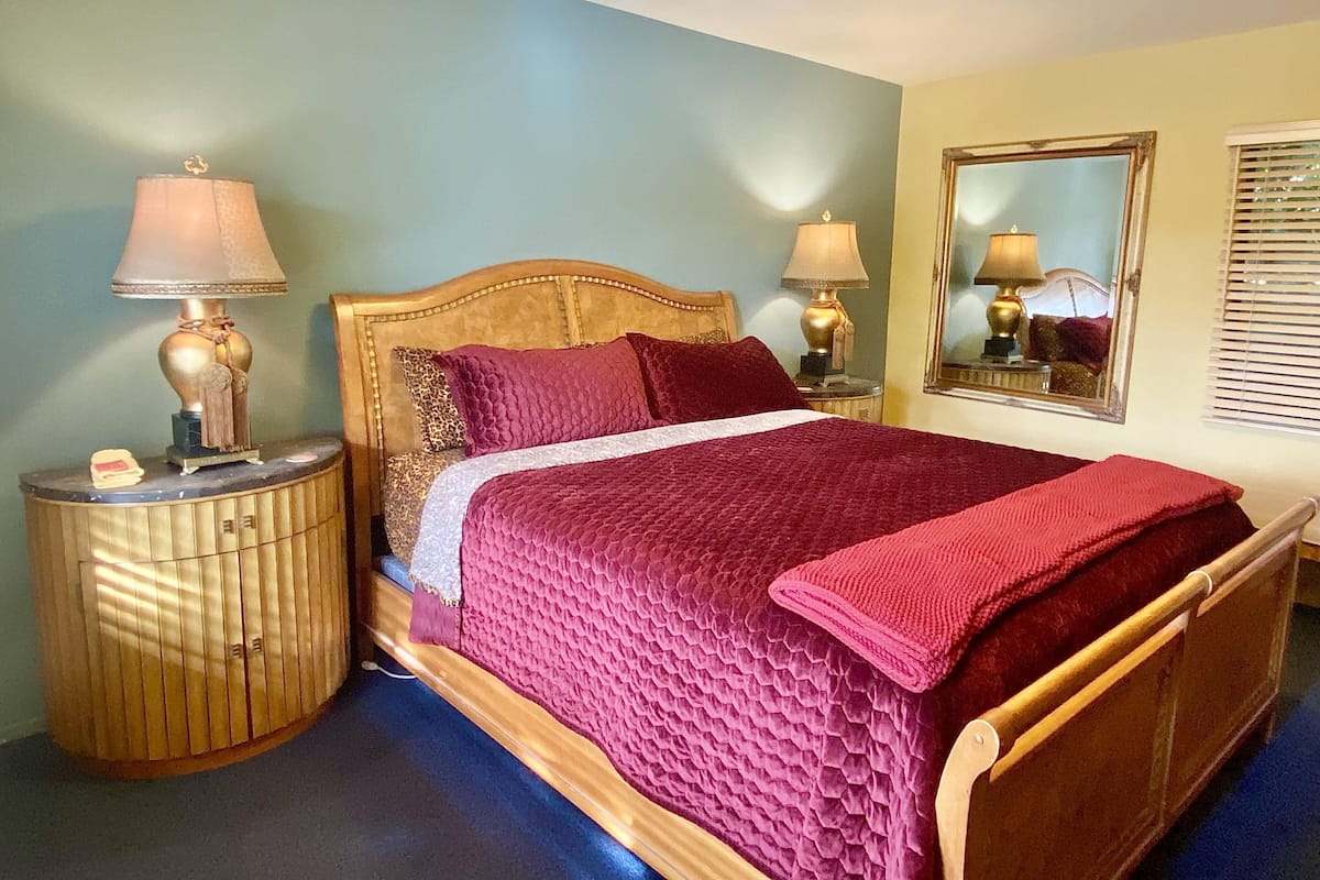 A neatly made bed with a wooden headboard, two bedside lamps, and a mirror on the wall.