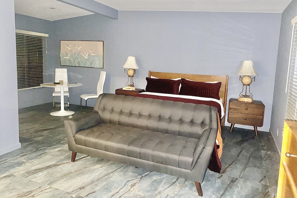 A bedroom with a bed, two bedside tables, a chair, a sofa, and a small table with a lamp.