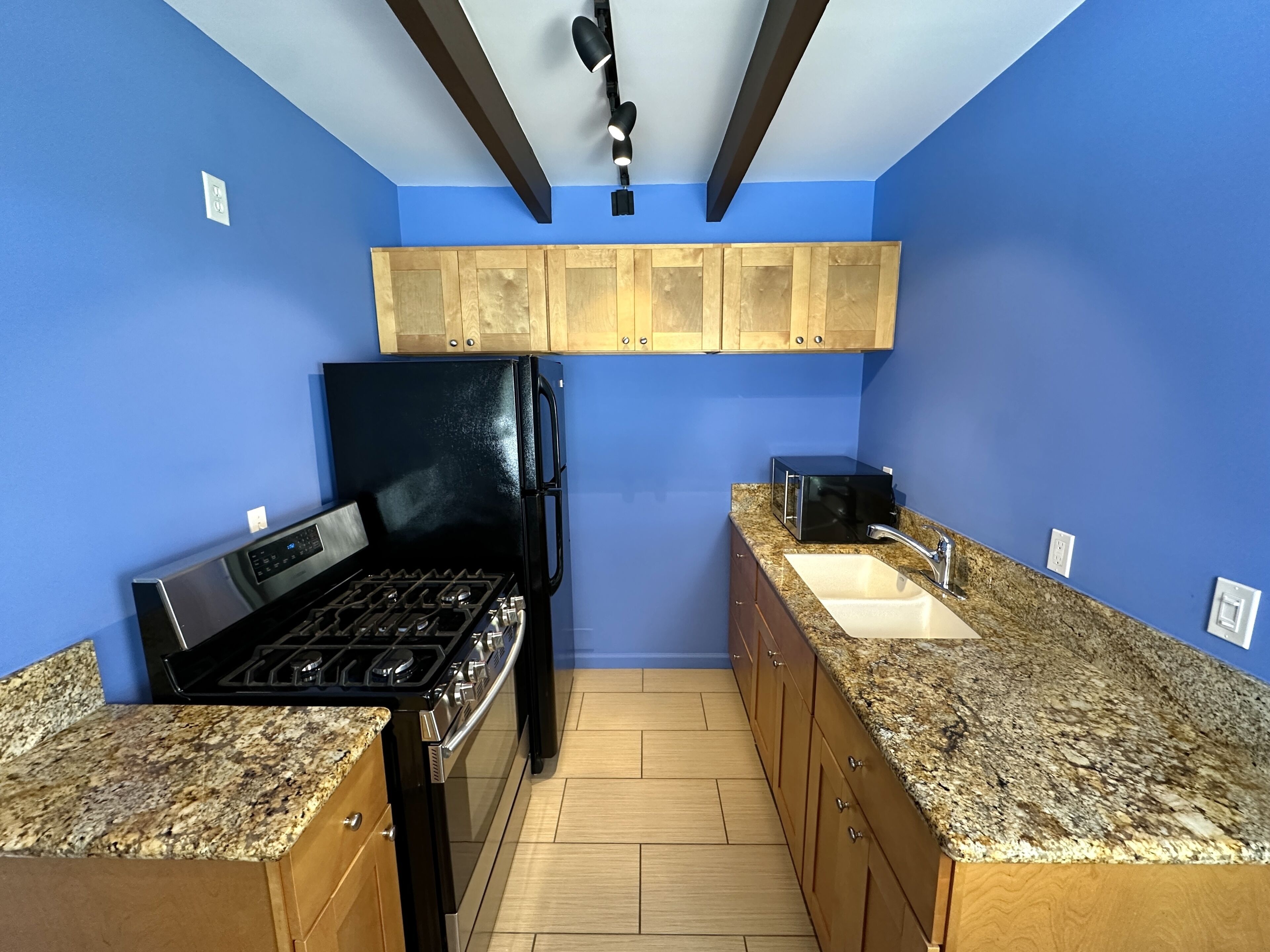 A kitchen with blue walls, wooden cabinets, a black refrigerator, a stove, granite countertops, and a sink.