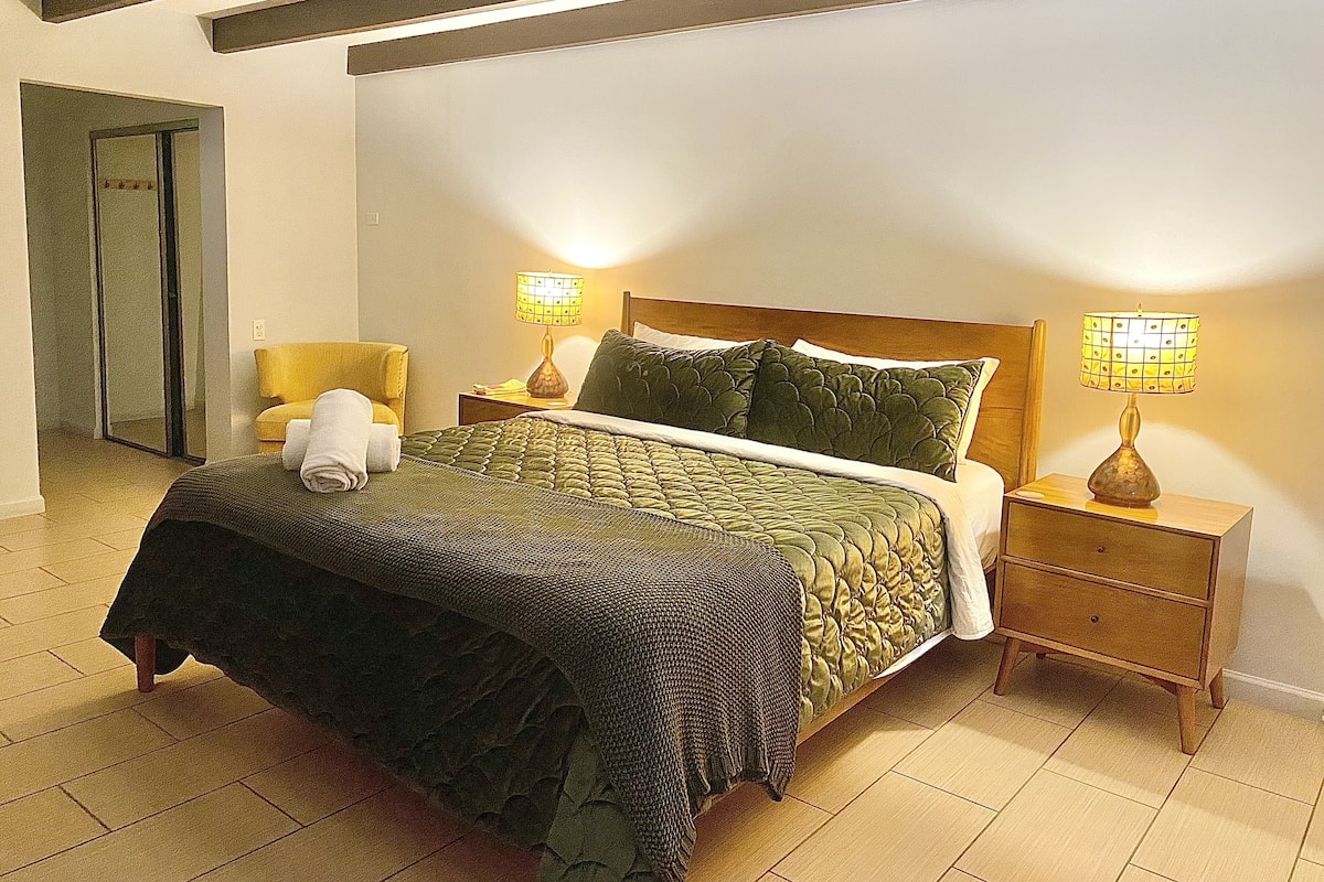 A neatly made bed with a green quilt, two bedside lamps, and a wooden nightstand.