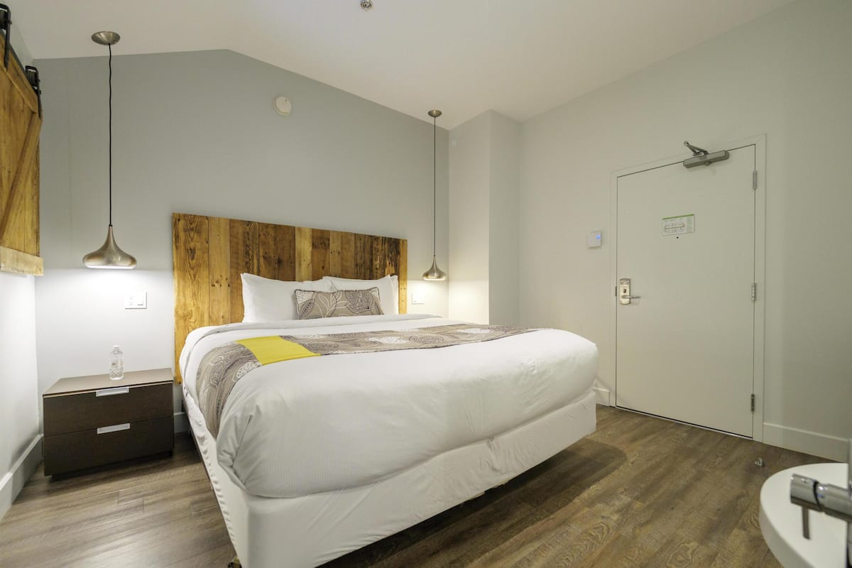 A bedroom with a wooden headboard, a bed with white bedding, a bedside table with a lamp, and a wooden floor.