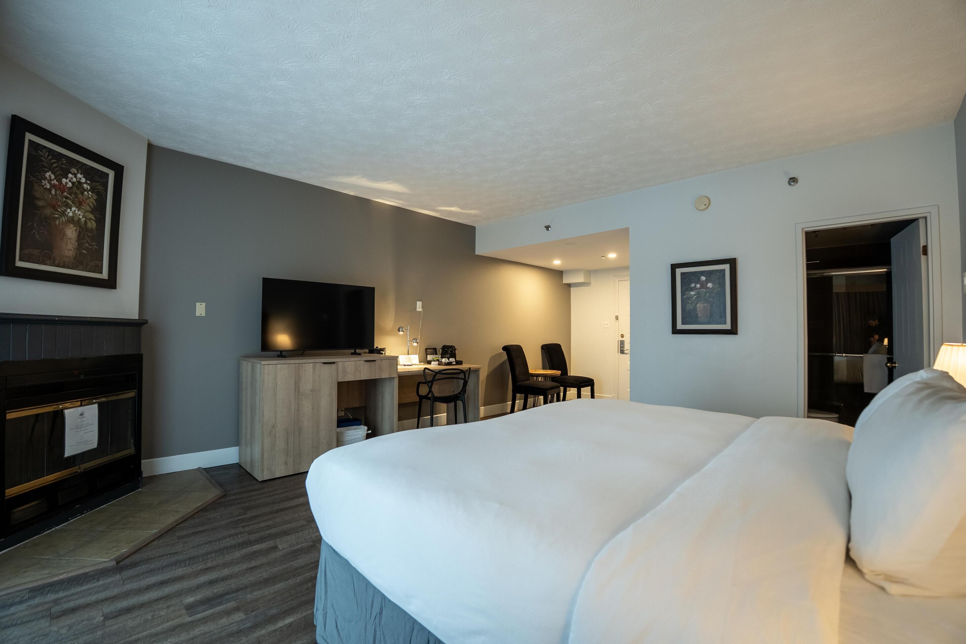 Habitación de hotel con una cama grande, un escritorio con silla, televisión y una puerta que da a otra habitación.